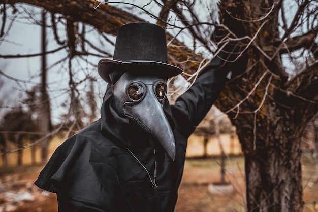 Plague doctor with a cane and a classic dark garb with a cross