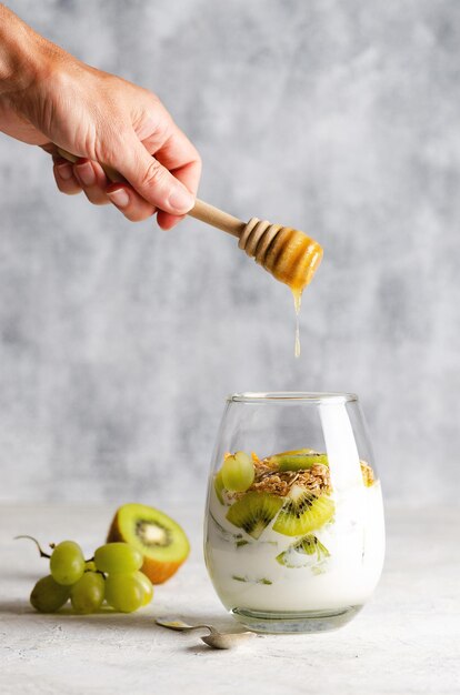 Plain yoghurt with pieces of fresh kiwi fruits white grapes granola and honey