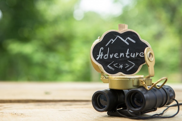 Plan your adventure concept Adventure written on a small sign compass and binocular outdoors green blurred background