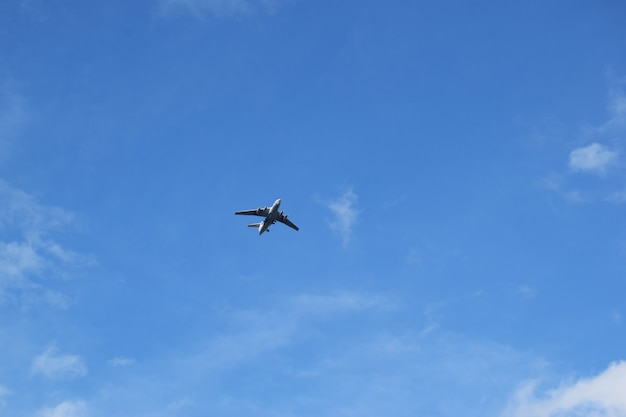 plane flies away into the distance against the blue sky with white clouds.