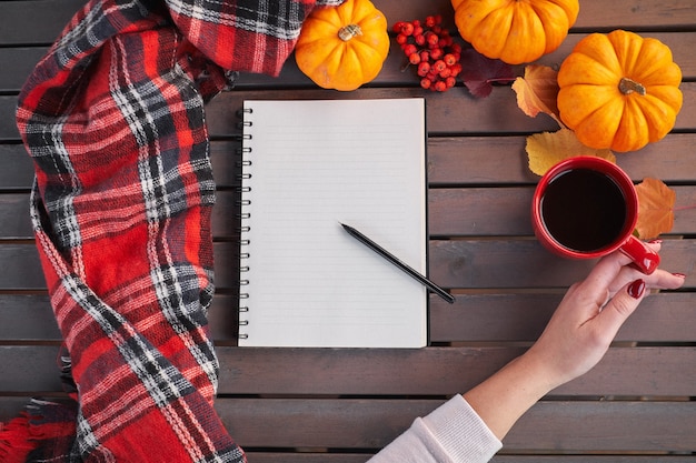 Planing to do list. Autumn mood composition on a wooden table. Young european girl with red manicure on nails holds in hands red cup, warming drink. Cozy atmosphere