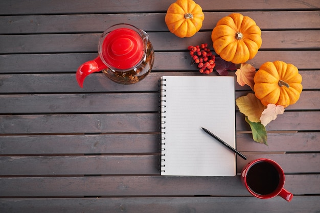 Planning to do list. Autumn mood composition on a wooden table with pumpkins, rowan and leaves. Open notepad and black coffee in the red cup and on grey wooden table, warming drink