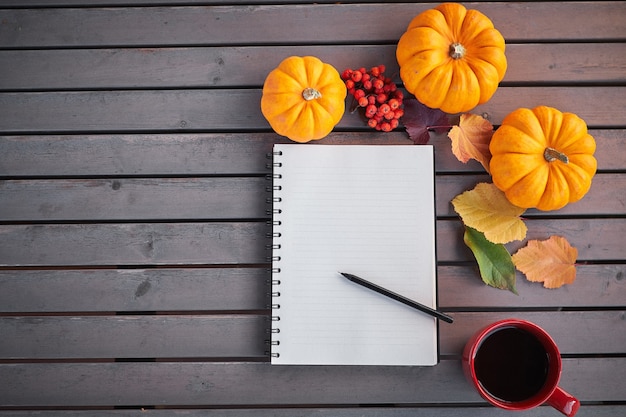 Planning to do list Autumn mood composition on a wooden table with pumpkins rowan and leaves. Open notepad and coffee in the red cup and on grey wooden table