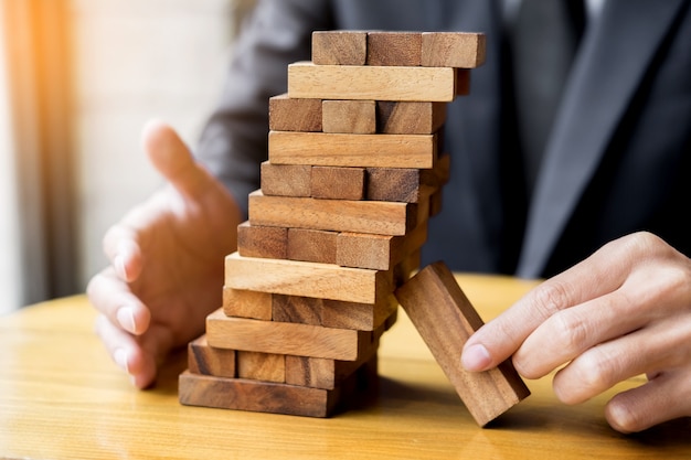 Planning, risk and wealth strategy in business concept, businessman and insurance gambling placing wooden block on a tower.