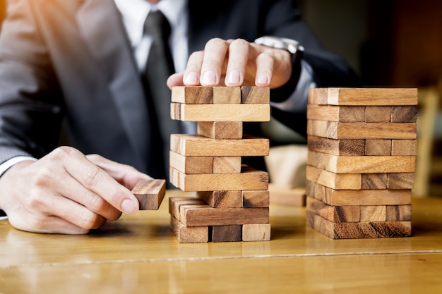 Planning, risk and wealth strategy in business concept, businessman and insurance gambling placing wooden block on a tower.