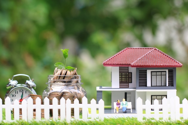 Plant growing on coins money in glass bottle with model house and miniature couple 