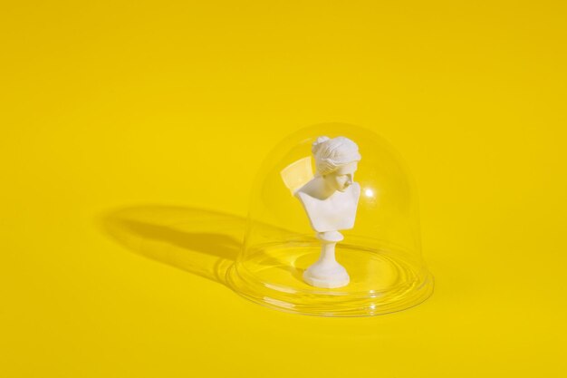 Plaster bust of venus under transparent dome on yellow background Protection isolation concept Minimal layout