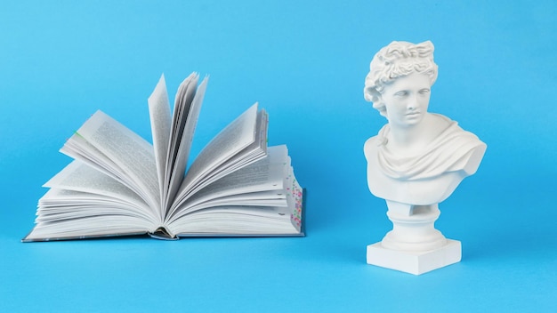 A plaster statuette and a large open book on a blue background Minimal concept