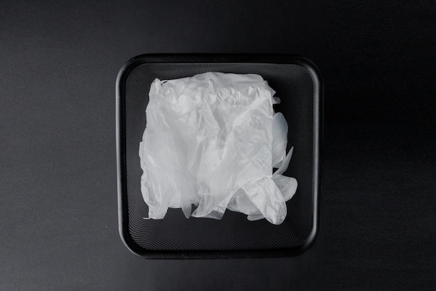 Plastic bag with handles gloves in the bin on a black background Used plastic bag for recycling Concept ecology planet pollution with plastic cellophane polyethylene