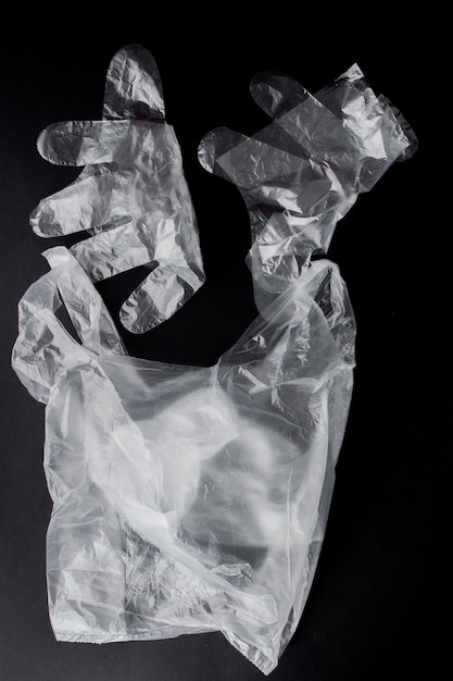 Plastic bag with handles, gloves, on a black background . Used plastic bag for recycling. Concept - ecology, planet pollution with plastic cellophane polyethylene