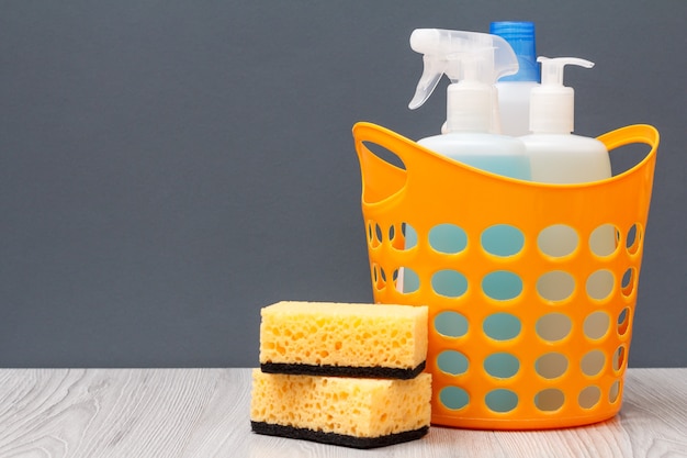 Plastic basket with protective glove, bottles of dishwashing liquid, glass and tile cleaner, detergent for microwave ovens and stoves, sponges on gray background. Washing and cleaning concept.