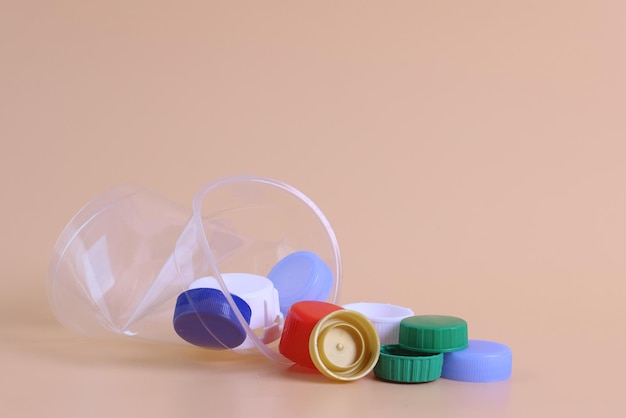 Plastic bottle caps with rumpled disposable cup on pastel background. Zero waste lifestyle concept.