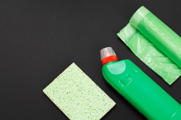 Plastic bottle of washing liquid a rag and garbage bags on the black background Top view