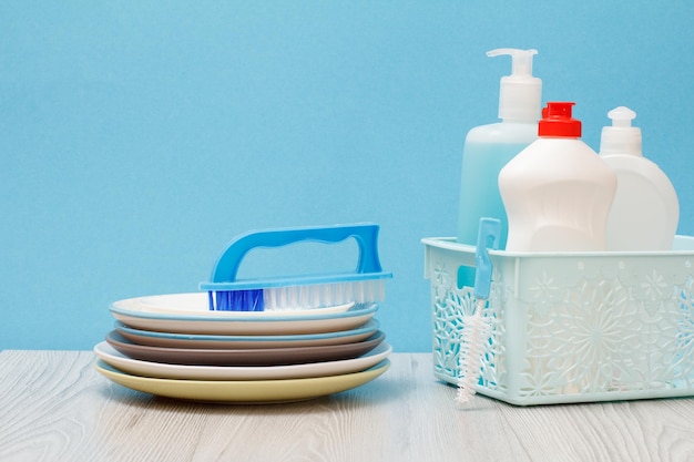 Plastic bottles of dishwashing liquid glass and tile cleaner in basket brushes clean plates