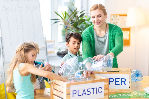 Plastic bottles. Teacher and children putting plastic bottles into box while sorting waste at the ecology lesson