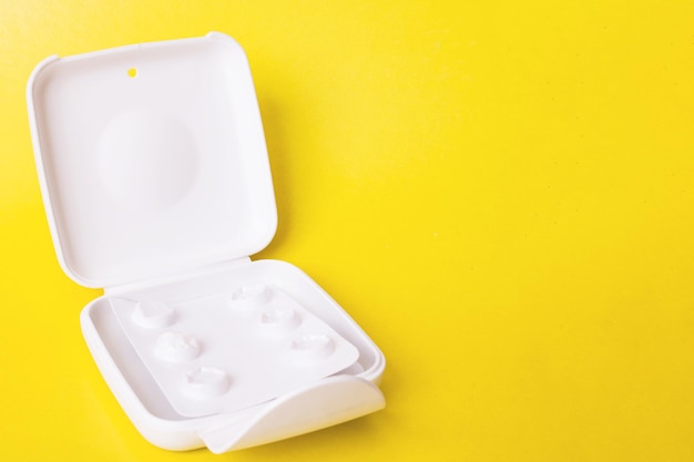 Plastic box with pills on yellow background