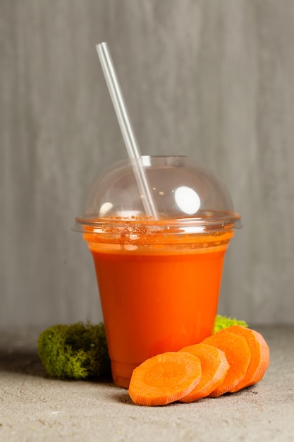 Plastic cup of carrot juice near with fresh vegetables