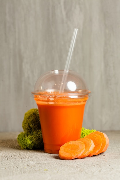 Plastic cup of carrot juice near with fresh vegetables