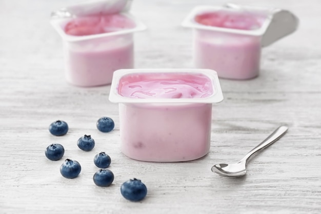 Plastic cup with yogurt and blueberries on wooden table