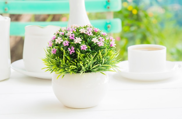 A plastic flower bouquet in a white spherical vase on a morning meal.