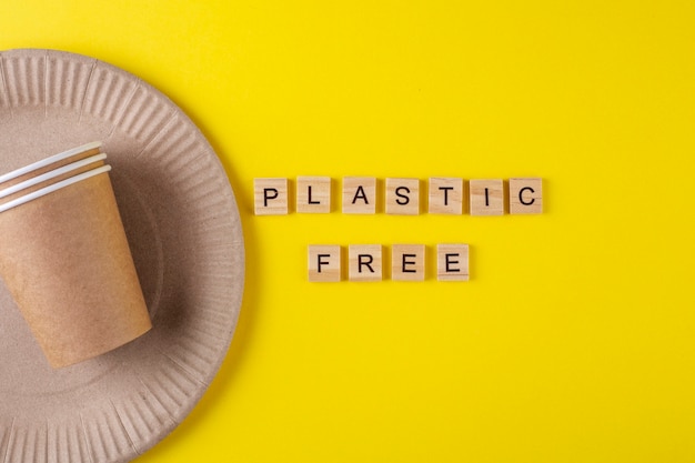 Plastic free inscription with paper plate and glasses on yellow surface