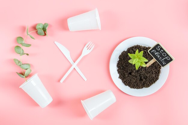 Plastic glasses forks knivesplate with earth a green sprout and a peg stop plastic on a pink