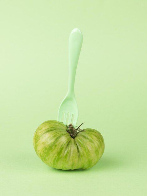 Plastic green fork in a green tomato on a green background