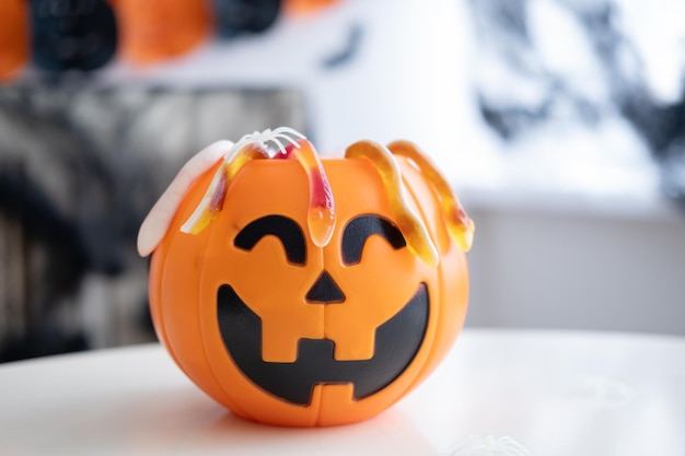 Plastic jack o lantern with marmalade on white table on halloween decorated background