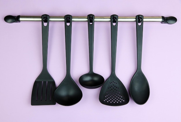 Plastic kitchen utensils on silver hooks on lilac background