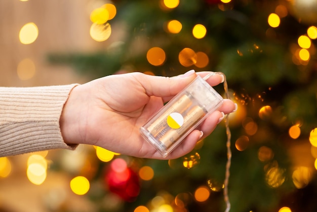 Plastic pack of garland with two AA batteries in hand of a girl Christmas tree on the background