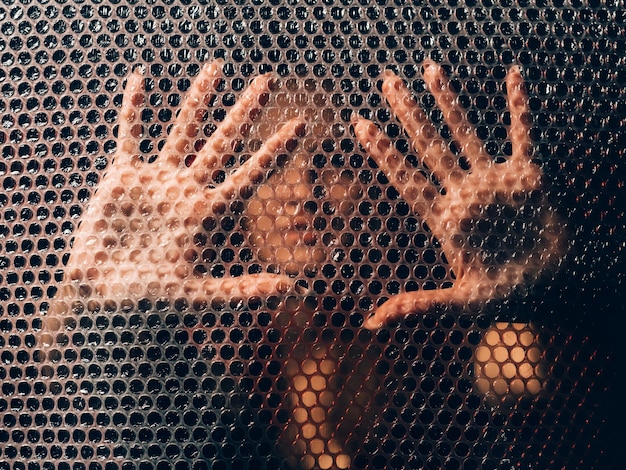 Plastic pollution. Waste recycling. Ecology problem. Textured art portrait of defocused scared woman silhouette touching polyethylene bubble wrap with hands wall on black blur background.