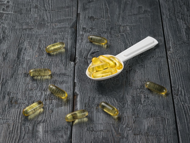 A plastic spoon with fish oil capsules on a wooden table