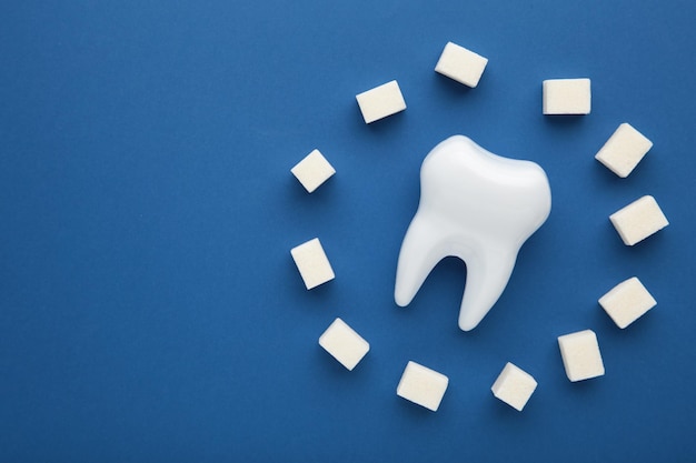 Plastic tooth with sugar on dark blue background Caries and sugar concept Dental care concept