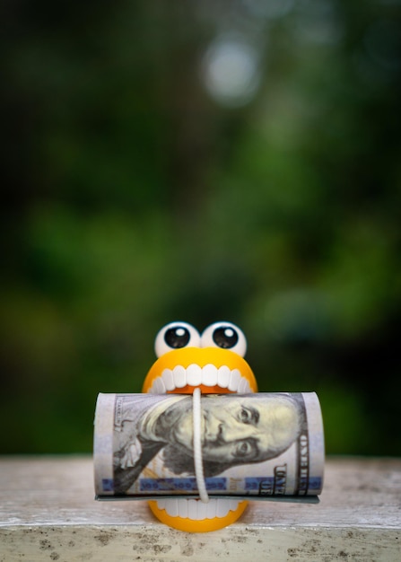 Plastic toy teeth with a roll of dollar banknote.