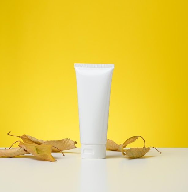 Plastic tube with a lid on a white table, yellow background. Packaging for cosmetics, branding and product promotion