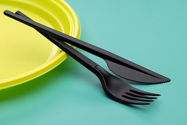 Plastic utensils close-up. Disposable yellow plate, black cutlery on a bright green background.