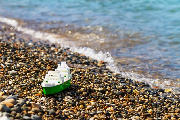 Plastic white-green toy boat at the seashore. Pebble beach.