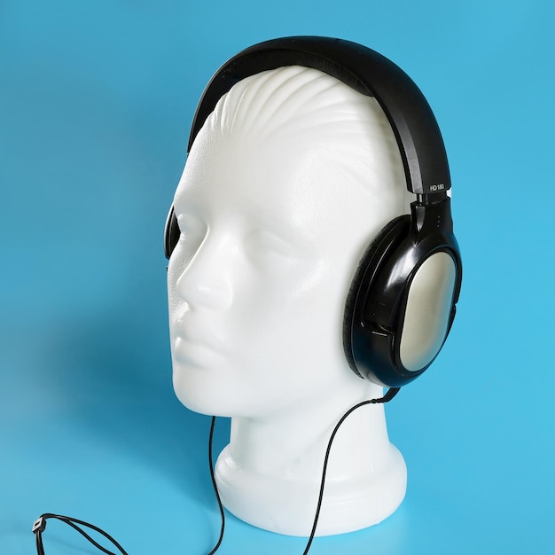 Plastic white mannequin head with musical stereo headphones on blue background