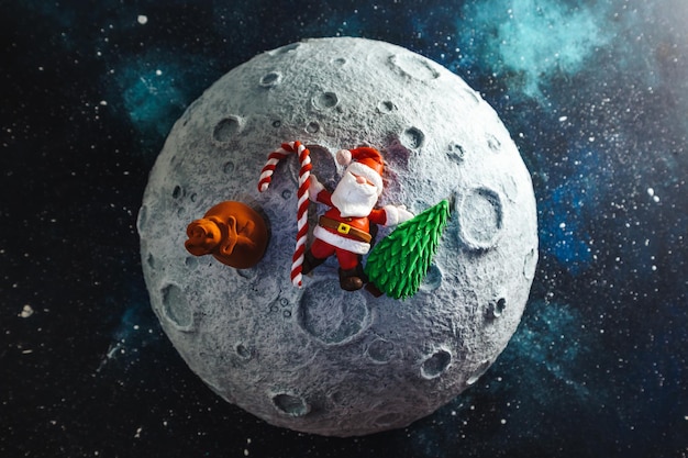 Plasticine Santa Claus lies on the moon with a bag of gifts and a Christmas tree