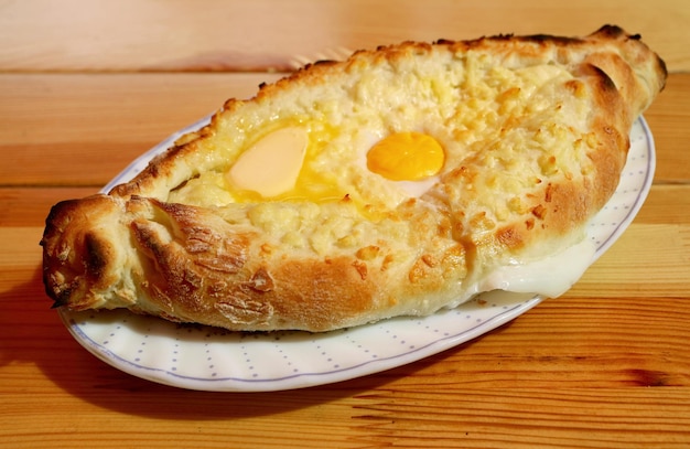 Plate of Adjaruli Khachapuri, Traditional Georgian Cheese and Egg Bread Served on Wooden Table