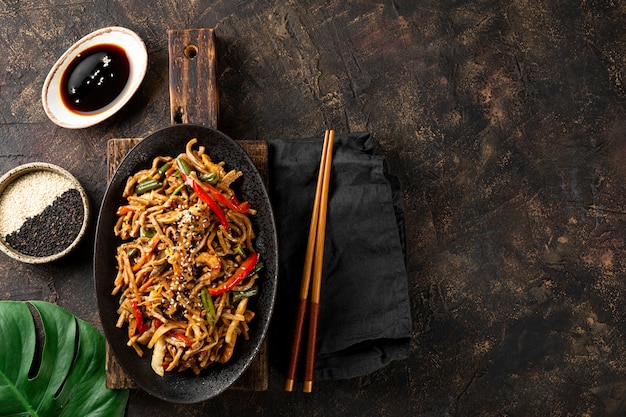 Plate of asian buckwheat soba noodles with vegetables mushrooms and chicken on dark background