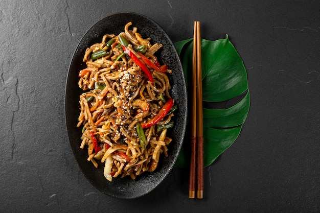 Plate of asian buckwheat soba noodles with vegetables mushrooms and chicken on dark background