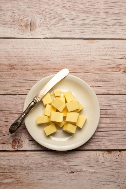 A plate of butter sits on a wooden table with a knife next to it.