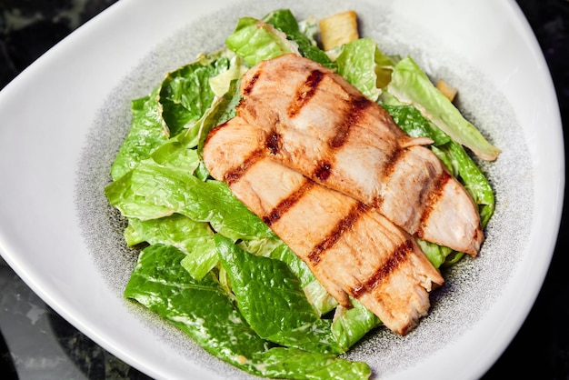 A plate of Caesar salad with chicken breast and parmesan