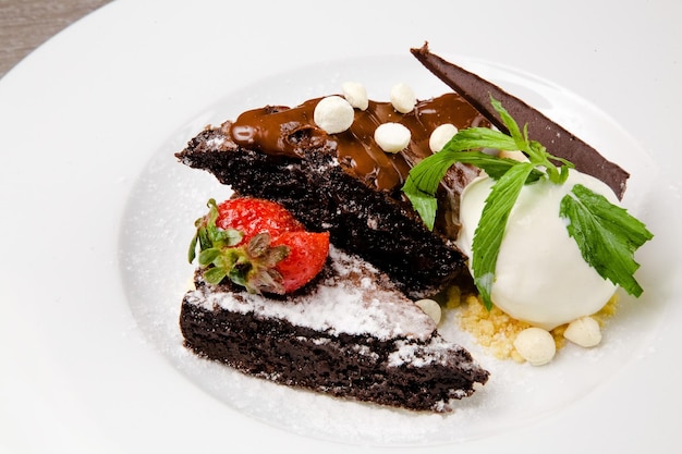 A plate of chocolate cake with a scoop of ice cream and a strawberry on top.