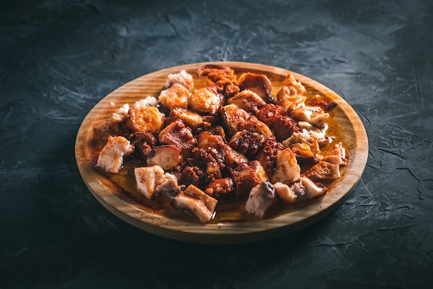 Plate of chopped octopus with oil and paprika in a round wooden plate on a dark table