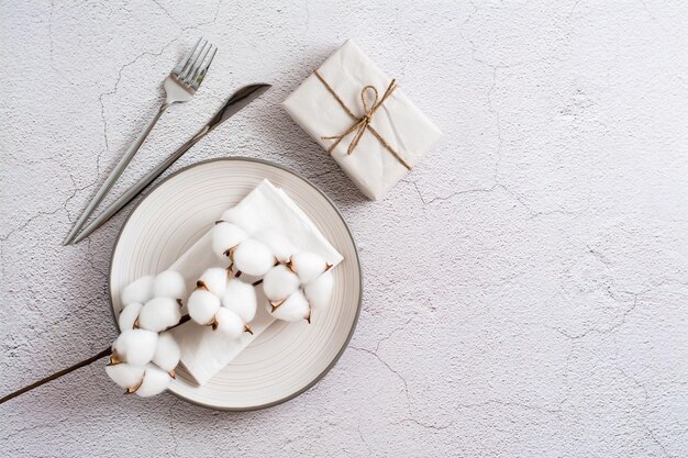 Plate cutlery gift and cotton branch on a textured gray background Eco serving Top view