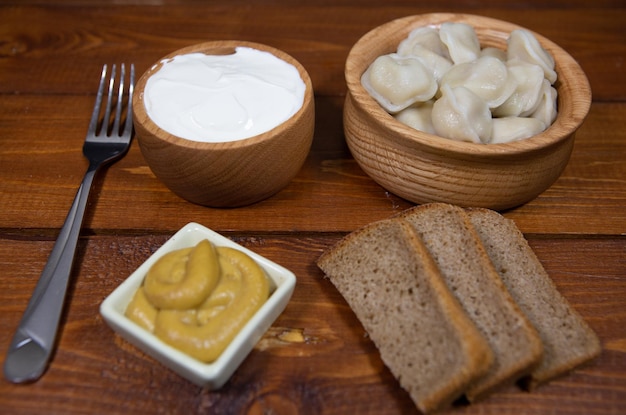 A plate of delicious boiled dumplings on a dark wooden table with various sauces and bread