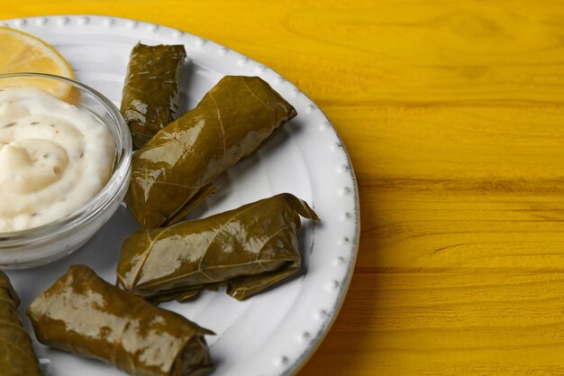 A plate of delicious stuffed Dolma with sauce and lemon on yellow wooden background