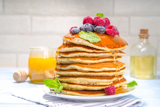 Plate of delicious traditional american pancakes with fresh berries and syrup on kitchen table on light background